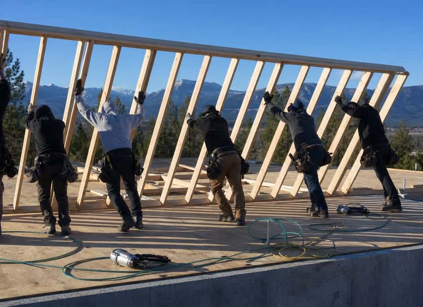 A framing crew standing an exterior stud wall upright on a new house deck in the Flathead Valley on a clear morning.