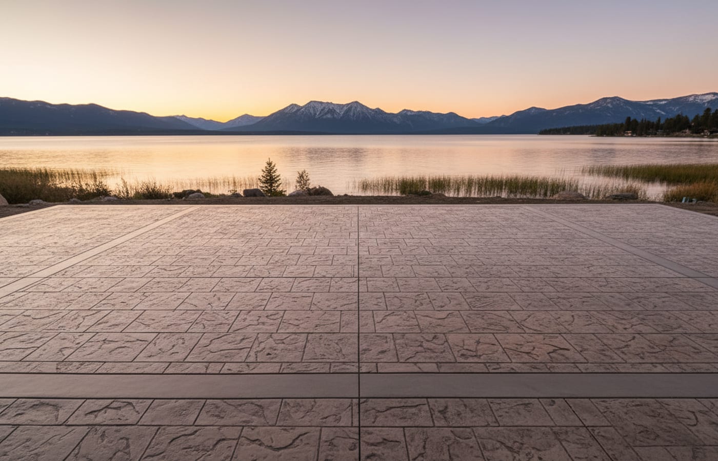 A finished stamped and coloured concrete patio in an ashlar slate pattern with a clean border band, lake and mountains beyond.